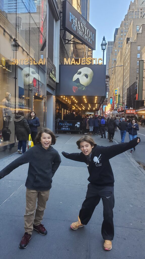 Two boys posing dramatically in front of the Majestic Theater marquee showing the Phantom of the Opera.