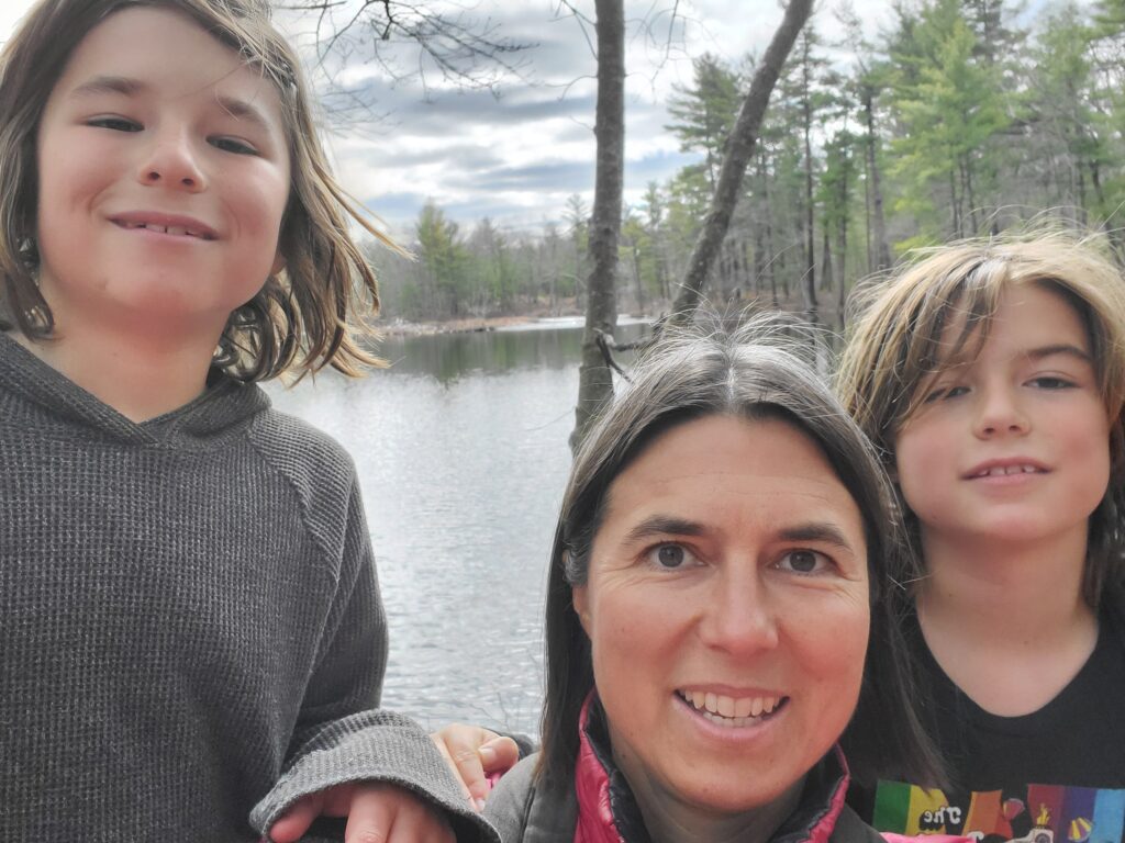Selfie of mom with twins with messy hair posing in front of a pond at Harold Parker State Forest.