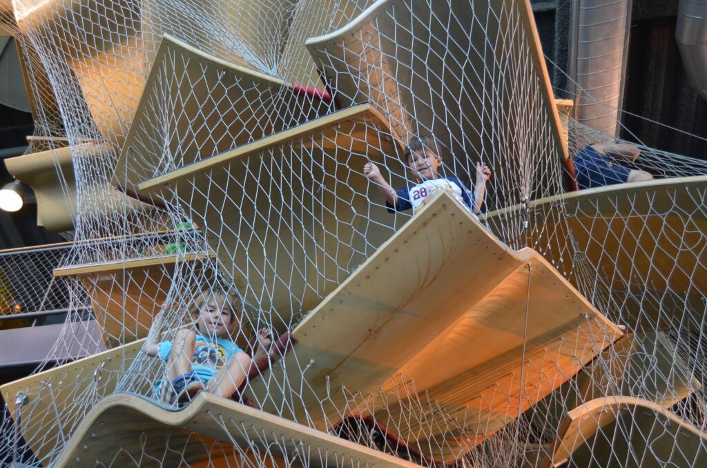 Two kids peeking out from the New Balance Climb at the Boston Children's Museum